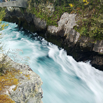 Fast flowing river in a deep gorge below a stone bridge.