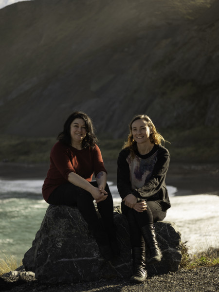 Writer Johanna Knox and photographer Jess Charlton sitting on a rock overlooking a beach