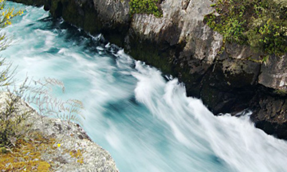 Fast flowing river in a deep gorge below a stone bridge.