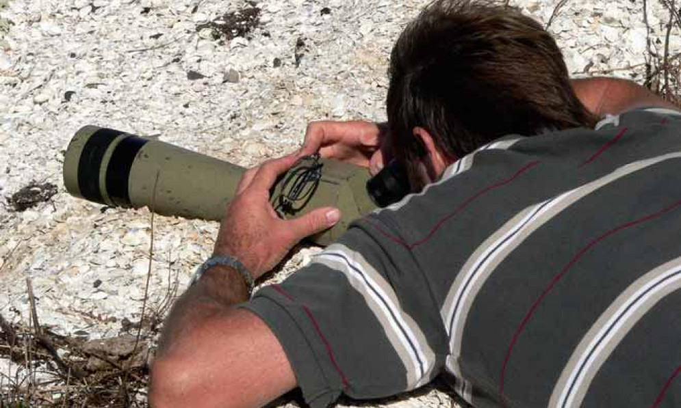 Man with camera lying on the ground to photograph birds