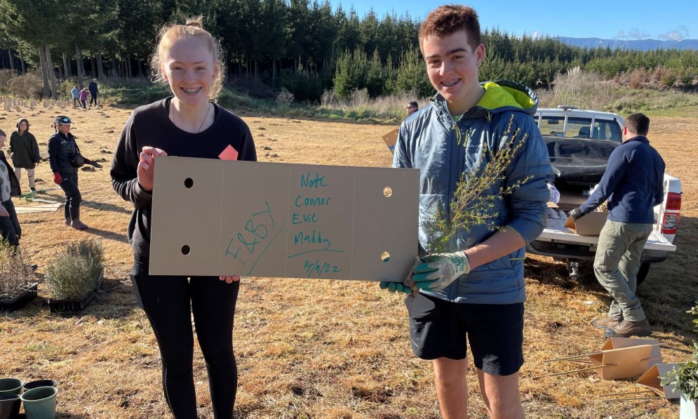 Evie and Nate marking the date of the Moturoa Rabbit Island community planting day on a cardboard tree protector. Credit Connor Wallace