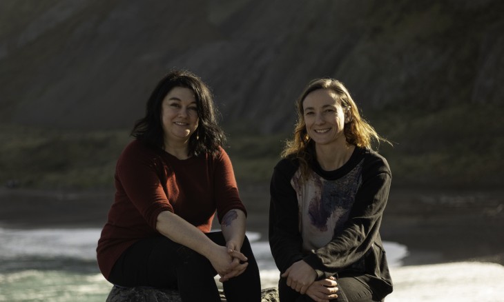 Writer Johanna Knox and photographer Jess Charlton sitting on a rock overlooking a beach