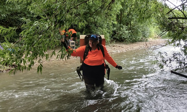 Former Te Hoiere team member Jessica Armstong crosses a river in Ronga Reserve to set up a new trapline. Credit Forest & Bird